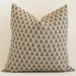 An attractive floral linen cushion in front of a white brick wall. It has a large shape and a sand colour.