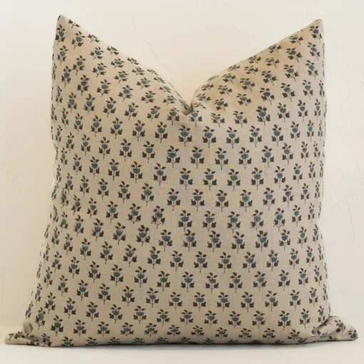 An attractive floral linen cushion in front of a white brick wall. It has a large shape and a sand colour.