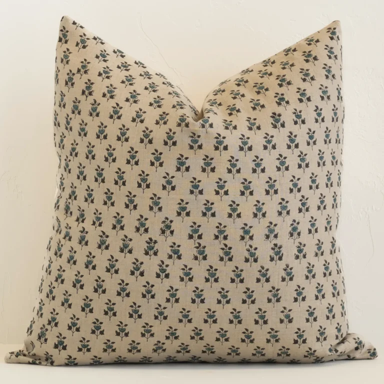 An attractive floral linen cushion in front of a white brick wall. It has a large shape and a sand colour.