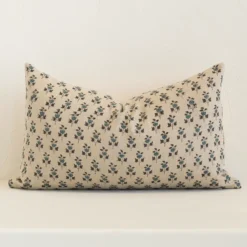 Sand-coloured floral cushion cover sits against a white wall. It is constructed from a superior looking linen material and has rectangle dimensions.
