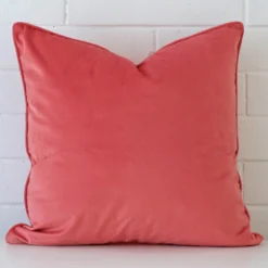A pretty velvet cushion cover is shown against a brick wall. It features a large shape and a coral colour finish.