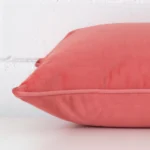 Side image of a velvet rectangle cushion cover. The design and coral colour are visible from the side showing the attachment of the panels.