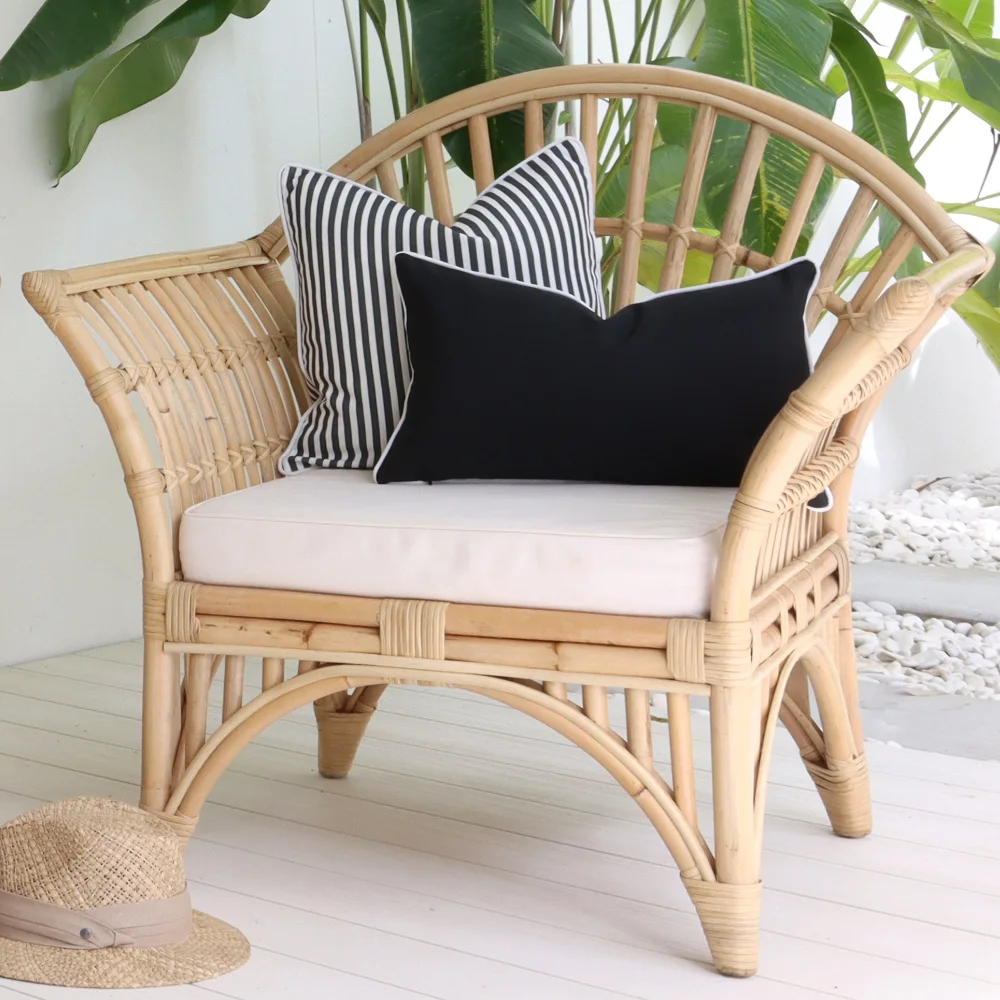 A curved outside rattan seat with two black outdoor cushions styled on it.