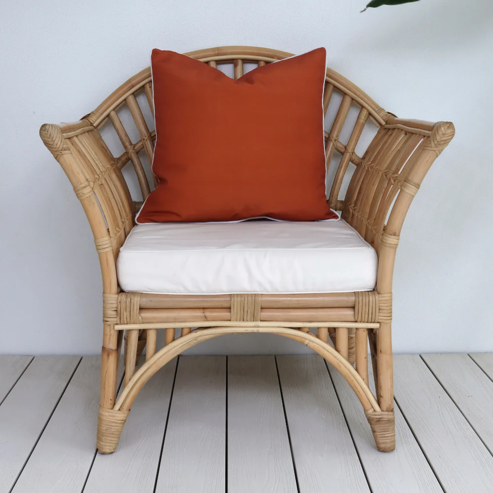 A curved rattan seat with a red outdoor cushion placed on it.