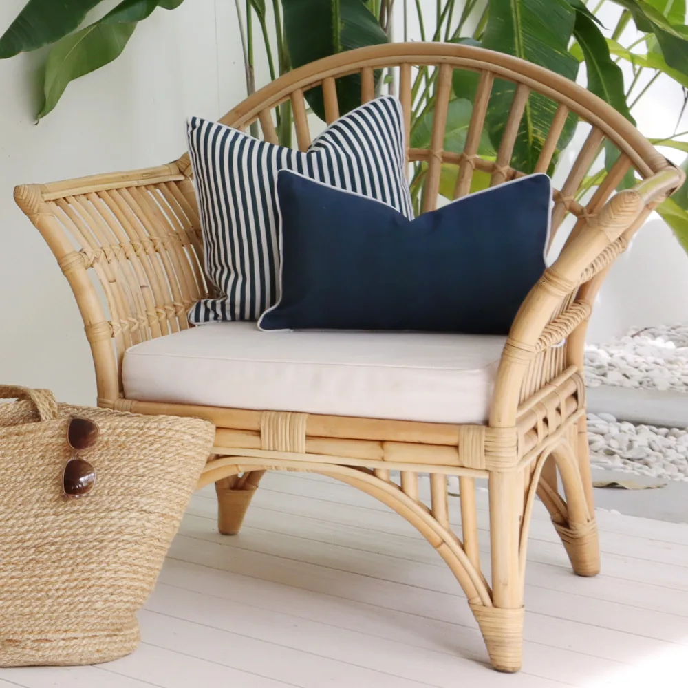 A curved single rattan seat with two blue outdoor cushions.