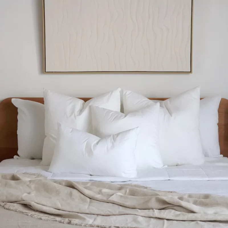cushion-insert-faux-feather-bed-set-of-4 Four cushion inserts are placed under a wall art decoration hanging on a bedroom wall.