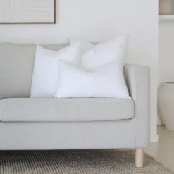 A set of 3 cushion inserts is arranged neatly on a corner of a grey sofa.
