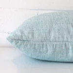 A duck egg cushion cover is laid flat. This angle shows the side of the linen fabric and its square shape.