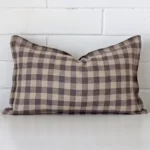 Here a designer cushion is shown styled against a white wall. It has a rectangle design and features a gingham style.