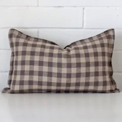 Here a designer cushion is shown styled against a white wall. It has a rectangle design and features a gingham style.