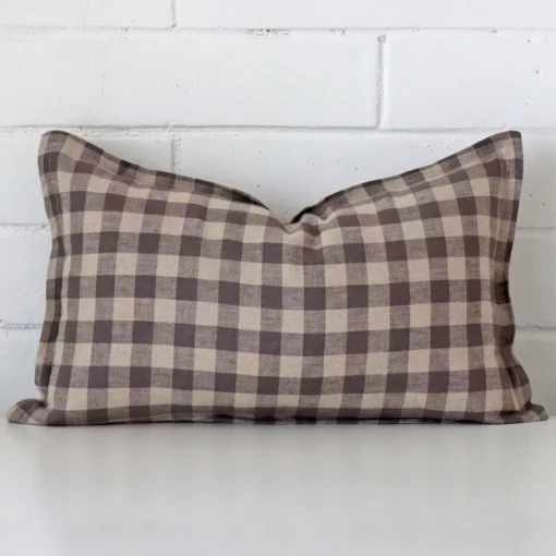 Here a designer cushion is shown styled against a white wall. It has a rectangle design and features a gingham style.