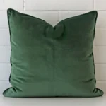 A lovely large dark sage cushion cover arranged in front of a white wall. It is made from a durable velvet material.