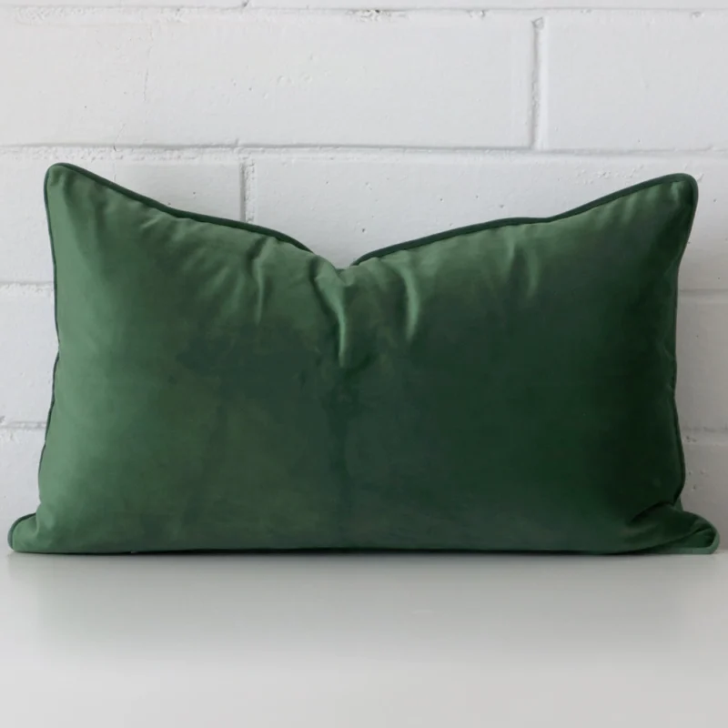 dark-sage-velvet-rectangular-cushion-cover-30cm-x-50cm-sc768-30 A rectangle cushion in a delightful dark sage tone rests against a white wall. The velvet material appears to be of exceptional quality.