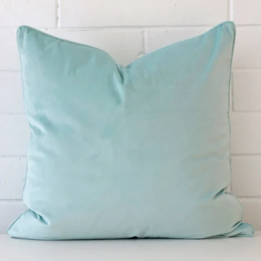 Duck eggcushion positioned in front of a brick wall. It has large dimensions and is made from a velvet material.