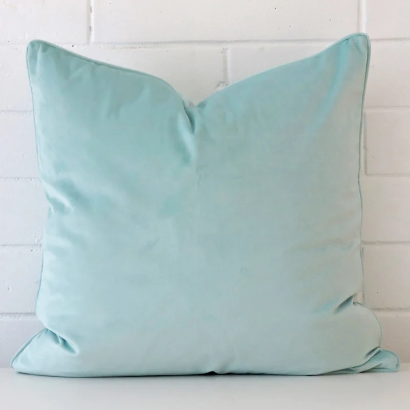 duck-egg-velvet-cushion-cover-55cm-x-55cm-sc772-55b Duck eggcushion positioned in front of a brick wall. It has large dimensions and is made from a velvet material.