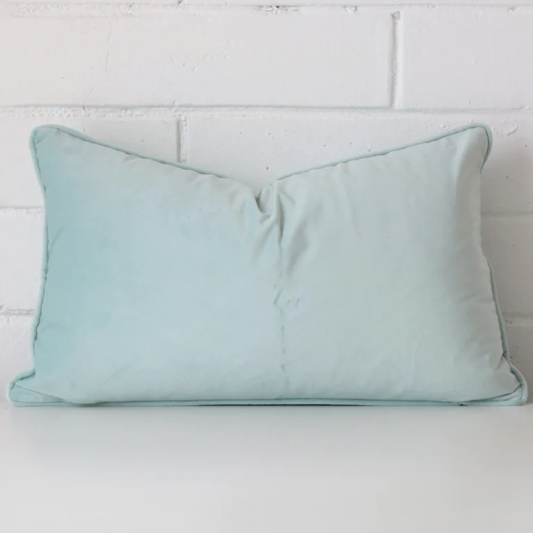 Duck egg cushion leans elegantly against a brick wall. It has been crafted from a high quality velvet material and has a square shape.
