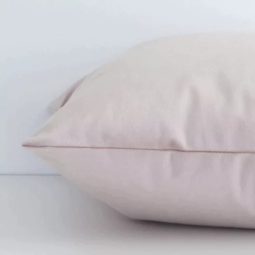 Square dusty pink cushion laid flat. This view shows the solid colour style and velvet fabric from side on.