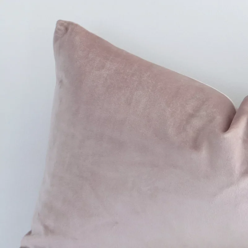 Rectangle solid-coloured cushion in dusty pink colour sitting upright in front of a white wall. It has been made from a quality velvet material.