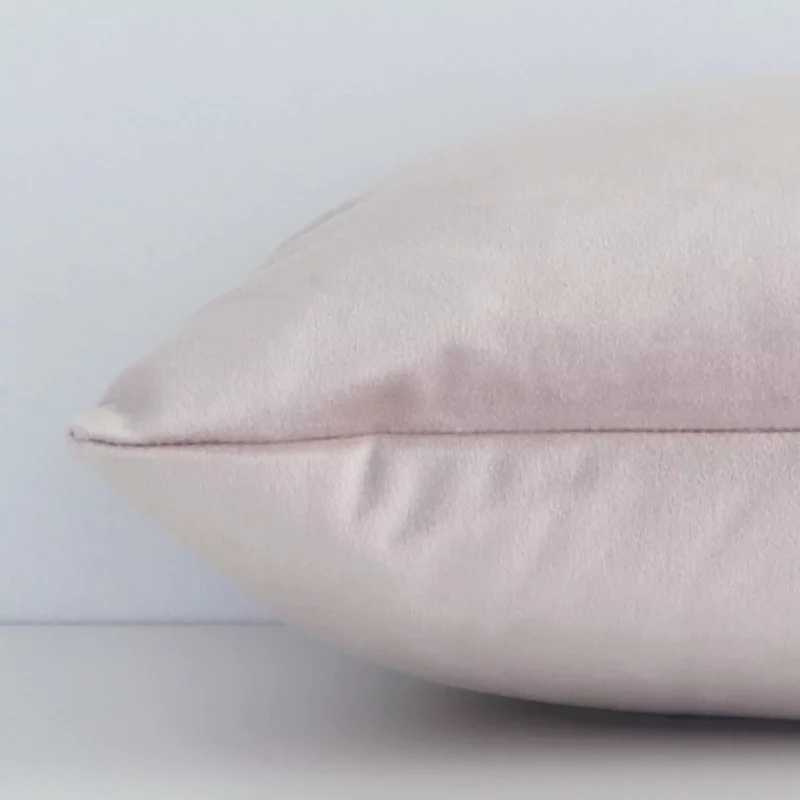 Dusty pink solid colour cushion cover laying sideways against white wall. The rectangle size and velvet material are shown highlighting the seams.