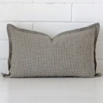 A designer rectangle cushion cover that has a unique gingham design is shown vertically against a brick wall.