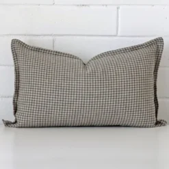 A designer rectangle cushion cover that has a unique gingham design is shown vertically against a brick wall.