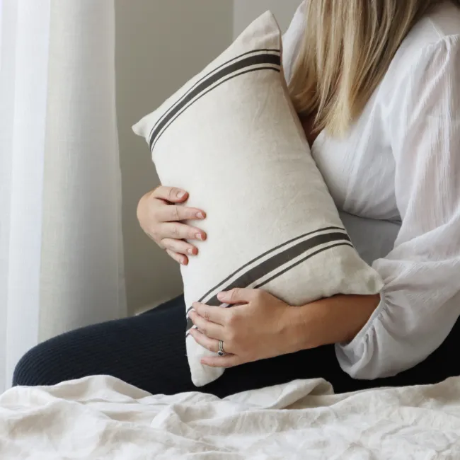 An elegant striped cushion is being held by a lady in her lap.