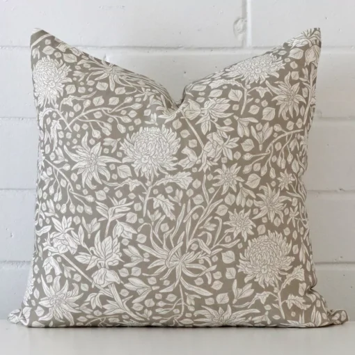A linen square cushion cover that has a unique floral design is shown vertically against a brick wall. It has a wonderful grey colour.