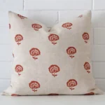 A large floral cushion in a delightful rust tone rests against a white wall. The linen material appears to be of exceptional quality.