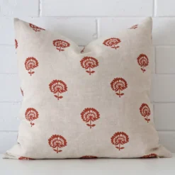 A large floral cushion in a delightful rust tone rests against a white wall. The linen material appears to be of exceptional quality.