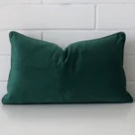 A pretty velvet cushion cover is shown against a brick wall. It features a rectangle shape and an emerald green colour finish.