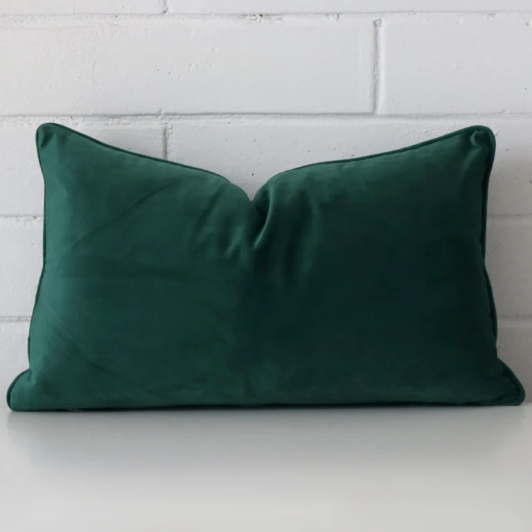 A pretty velvet cushion cover is shown against a brick wall. It features a rectangle shape and an emerald green colour finish.