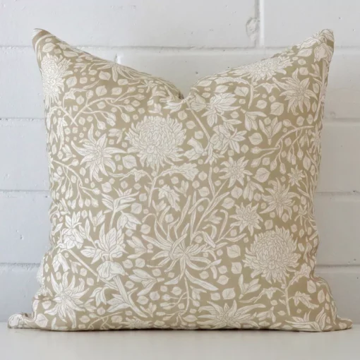 A square floral cushion in a delightful tone rests against a white wall. The linen material appears to be of exceptional quality.