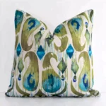 An attractive patterned linen cushion in front of a white wall. It has a square shape and is colourful.
