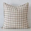 Here a designer cushion is shown styled against a white wall. It has a large size and features a gingham style.