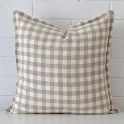 Here a designer cushion is shown styled against a white wall. It has a large size and features a gingham style.