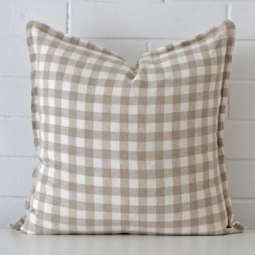 Here a designer cushion is shown styled against a white wall. It has a large size and features a gingham style.