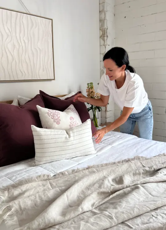 Four cushions being styled on bed by a woman in a white shirt.