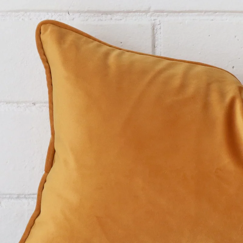 A velvet rectangle cushion’s corner has been enlarged in this shot. It has a gold mustard colour.