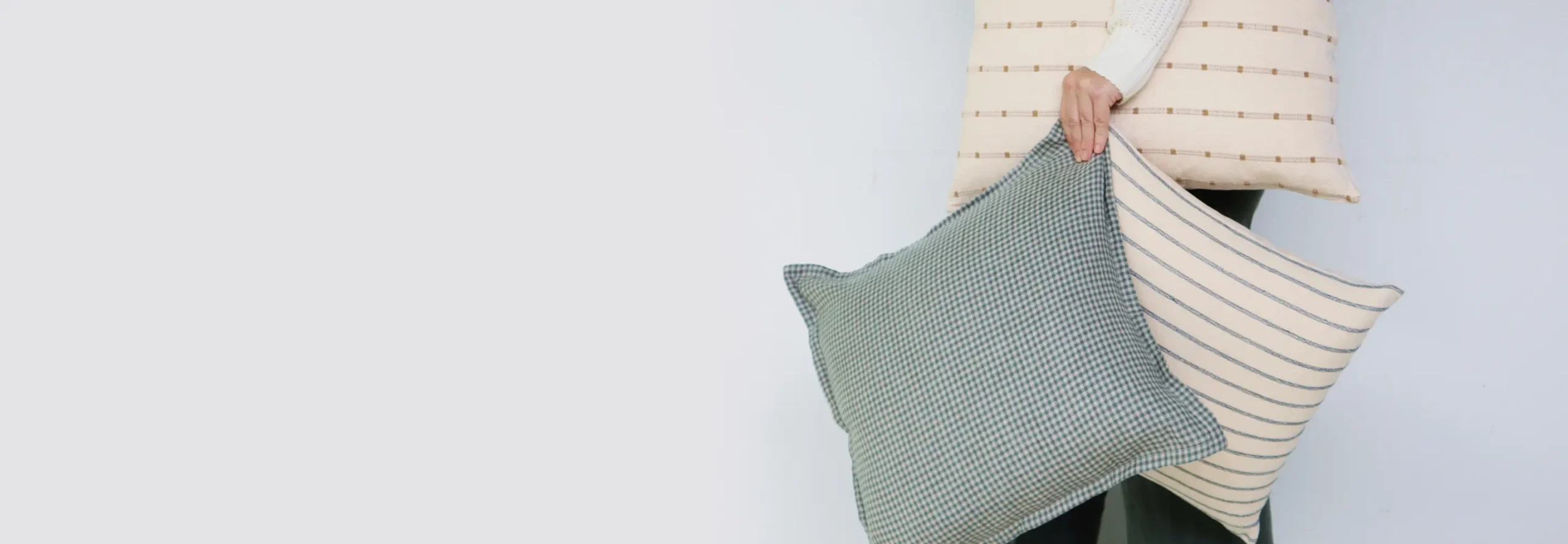 A hand is holding some cushions and cushion covers against the backdrop of a light wall.