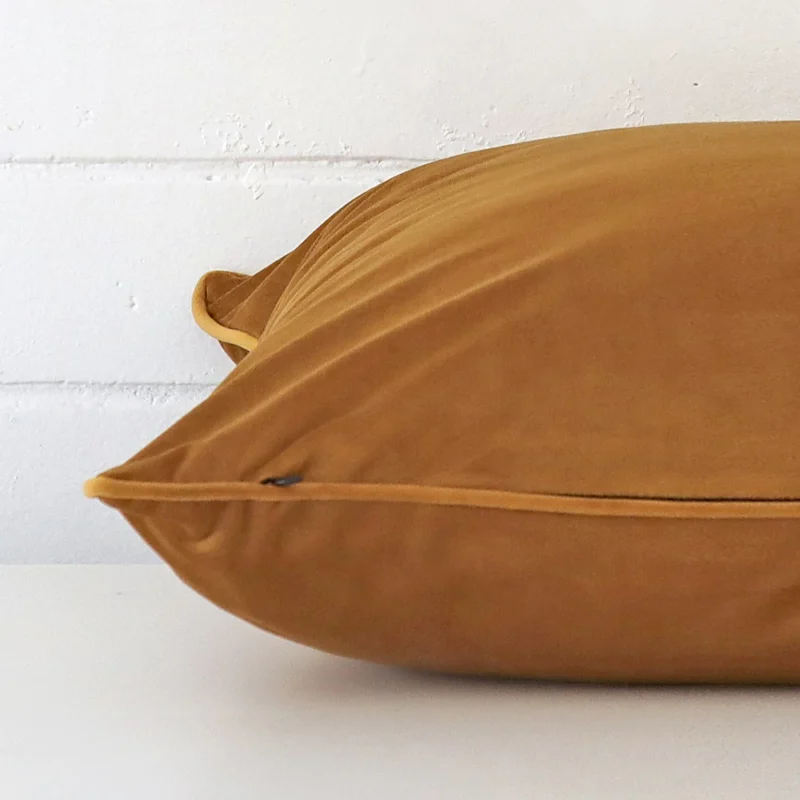 A honey mustard cushion cover is laid flat. This angle shows the side of the velvet fabric and its large size.