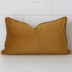 A lovely rectangle honey mustard cushion cover arranged in front of a white wall. It is made from a soft velvet material.
