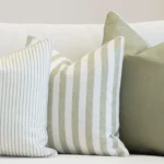 A set of 3 outdoor couch cushions in a horizon sage colour are displayed on a white couch.