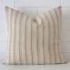 A brick wall that has a striped cushion cover positioned in front of it. It has an exquisite designer material and a lovely large shape.