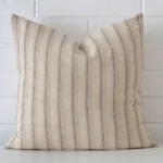 A brick wall that has a striped cushion cover positioned in front of it. It has an exquisite designer material and a lovely large shape.