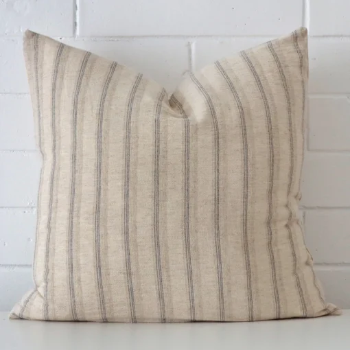 A brick wall that has a striped cushion cover positioned in front of it. It has an exquisite designer material and a lovely large shape.