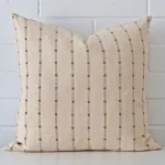 Striped cushion leans elegantly against a brick wall. It has been crafted from a high quality designer material and has a large size.