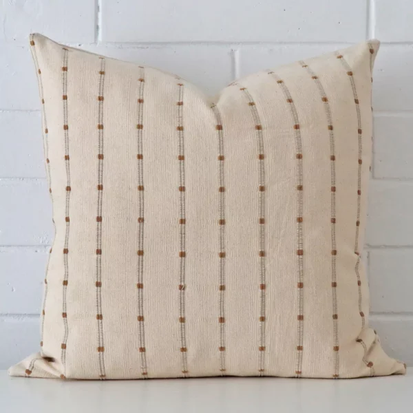 Striped cushion leans elegantly against a brick wall. It has been crafted from a high quality designer material and has a large size.