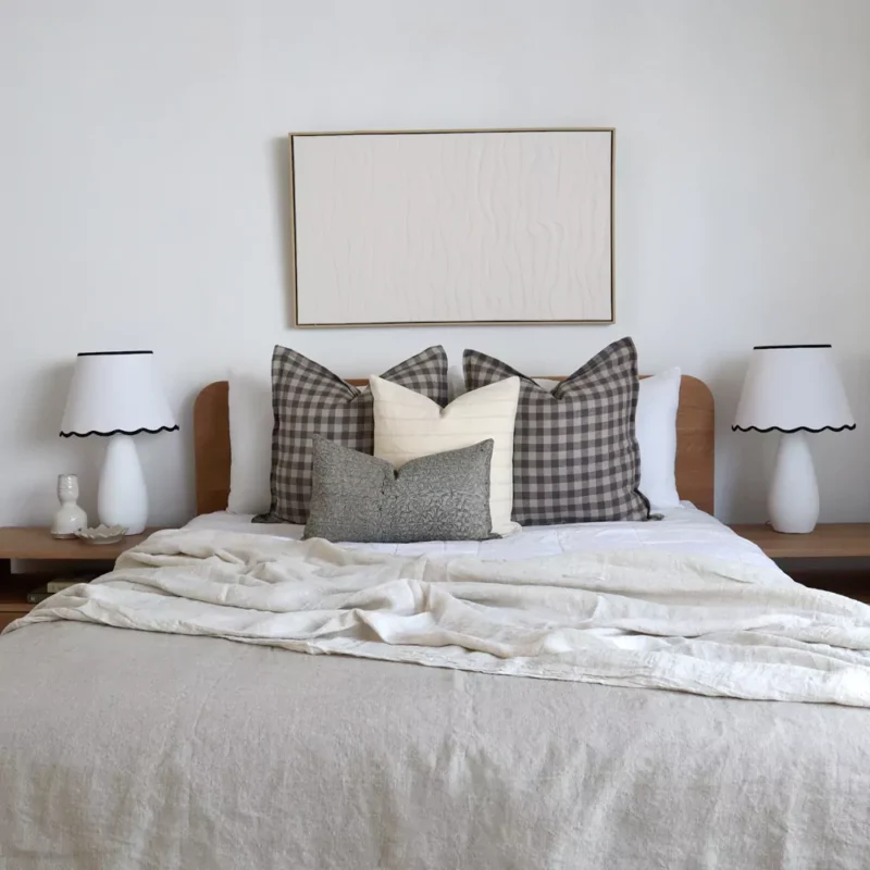 A set of 4 designer bed cushions on a wooden bed between two white lampshades.