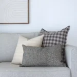 3 designer couch cushions are sitting in the corner of grey sofa.