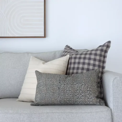 3 designer couch cushions are sitting in the corner of grey sofa.